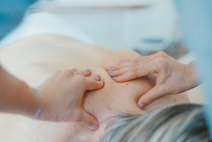 Therapist's hands massaging a client's upper back during a back massage session.