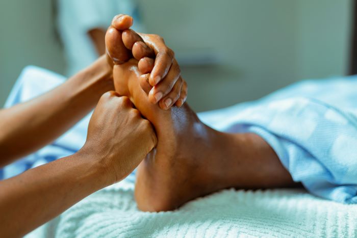 Caregiver massaging a patient's foot in a clinical or spa setting, hands gently holding the foot above a soft towel-lined surface