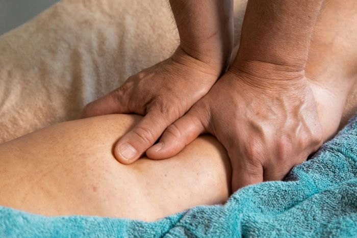 Close-up of a massage therapist's hands pressing into a person's leg, resting on a teal towel.